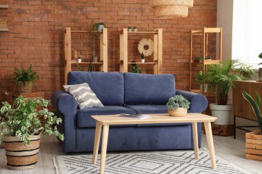 Oturma odasının içinde kanepe, raf üniteleri, masa ve ev bitkileri var.