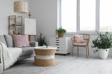 Konforlu kanepesi, göğüs çekmecesi, masası, çiçekleri, raf üniteleri, koltuğu ve sehpası olan bir oturma odası.