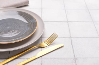 Temiz tabaklar ve beyaz karo zemin üzerinde altın çatal bıçak seti ile masa ayarları