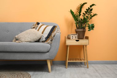 Şeftali duvarının yanındaki taburede yastıklı, çiçekli ve küp takvimli gri kanepe.