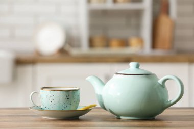 Güzel çaydanlık, bir fincan sıcak çay ve limon dilimi mutfaktaki ahşap masada.