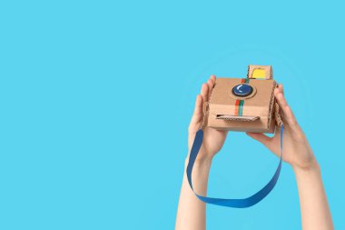 Mavi arka planda fotoğraf makinesi olan kadın eller.