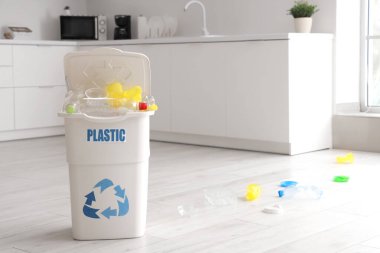 PlaSTIC yazısıyla dolu çöp kutusu ve mutfakta yerde çöp. Geri dönüşüm kavramı