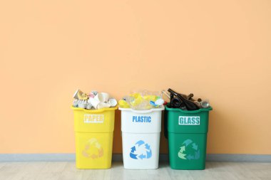 Bej duvarın yanında farklı türde çöp kutuları var. Geri dönüşüm kavramı