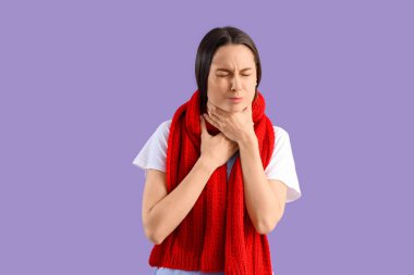 Leylak arka planında boğaz ağrısı çeken fularlı genç bir kadın.