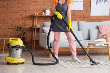 Evde elektrikli süpürgeyle halı temizleyen genç bir kadın.