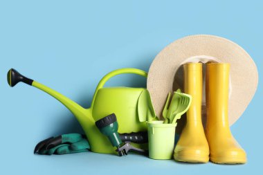 Sulama kutusu, lastik botlar ve mavi arka planda şapkası olan kompozisyon. Bahçe araçları