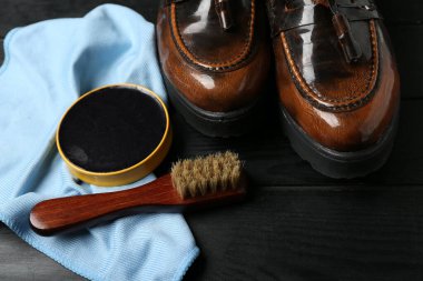 Siyah ahşap arka planda parlak deri ayakkabılar, kumaş, fırça ve ayakkabı cilası.