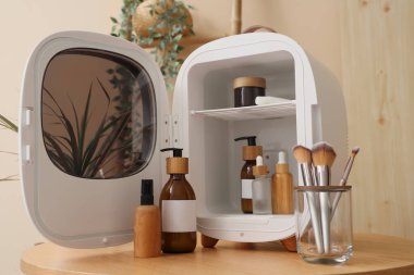 Küçük buzdolabı olan ahşap masa, fırçalı tutucu ve ışık duvarının yanında kozmetik ürünler.