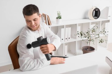 Genç işadamı masadaki perküsyon masajıyla omzuna masaj yapıyor.