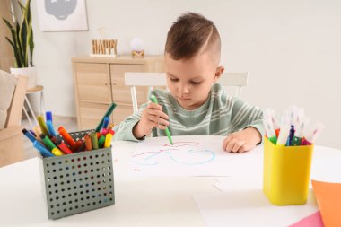 Evdeki masada keçeli kalemle çizen komik küçük çocuk.