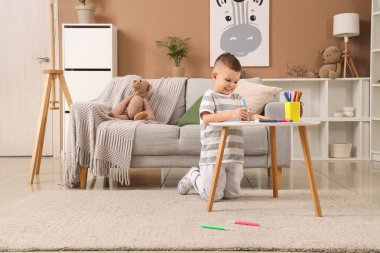 Evdeki masada keçeli kalemlerle resim çizen sevimli küçük çocuk.