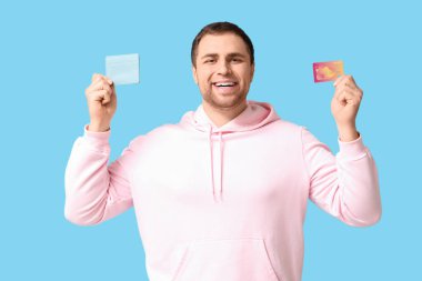 Mavi arka planda cüzdan ve kredi kartı tutan mutlu genç adam.