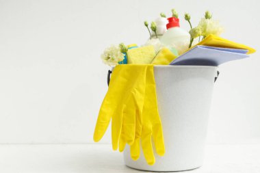 Beyaz arka planda temizlik malzemeleri, aletler ve bahar çiçekleriyle dolu kova