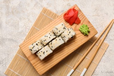 Gri grunge arka planında lezzetli suşi dürümleri, yemek çubukları ve bambu paspası olan tahta.