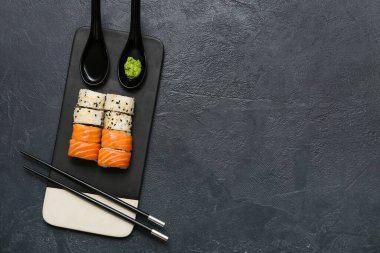 Lezzetli suşi ruloları, yemek çubukları ve siyah grunge arka planda wasabi olan tahta.