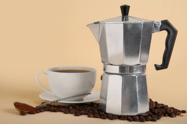 Bej arka planda fincanı, kaşığı ve fasulyesi olan gayzer kahve makinesi.