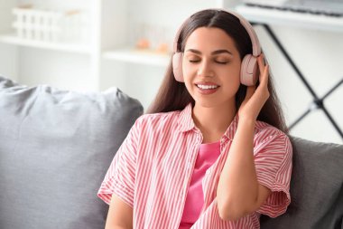 Güzel, genç, mutlu, kulaklıklı bir kadın evde müzik dinliyor.