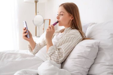 Evde cep telefonu kullanan ve elektronik sigara içen genç bir kadın.