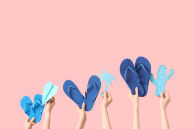 El ele tutuşan üç çift parmak arası terlik kağıt uçak, avuç içi ve kaktüs pembe arka planda.