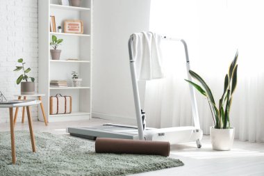 Oturma odasının iç tarafında havlu ve spor paspası olan koşu bandı.