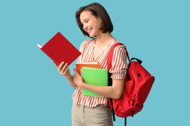 Sırt çantası ve mavi arka planda defterleri olan güzel bir kız öğrenci.