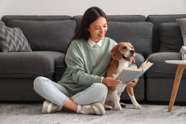 Genç bir kadın kitap okuyor ve oturma odasında yerde sevimli bir tazı köpeğiyle oturuyor.