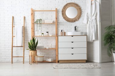 Çekmeceler, lavabo ve raf ünitesi. Banyoda beyaz tuğla duvarın yanında havlu var.