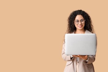 Kahverengi arka planda modern dizüstü bilgisayarı olan genç bir Afro-Amerikalı iş kadını.