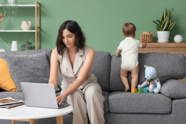 Evde doğum izninde dizüstü bilgisayarla çalışan tatlı bebek ve genç anne.