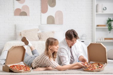 Güzel genç çift, yatak odasında lezzetli pizzalarla halı ve karton kutularda yatıyor.