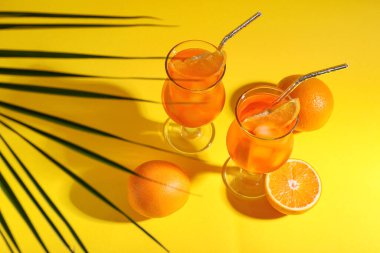 Sarı arka planda Aperol spreyli kokteyl ve palmiye yaprağı.
