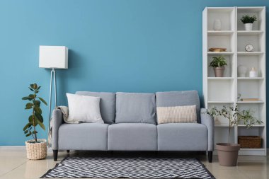 Rahat bir kanepe, ev bitkisi ve mavi duvarın yanındaki raf ünitesi.