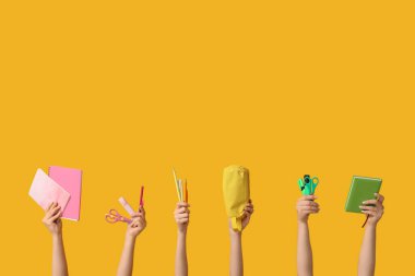 Sarı arka planda farklı kırtasiye malzemesi olan kadın elleri