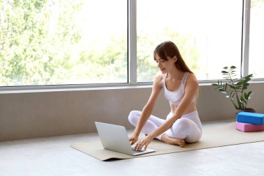 Sabahları evde yoga yaparken dizüstü bilgisayar kullanan genç bir kadın.