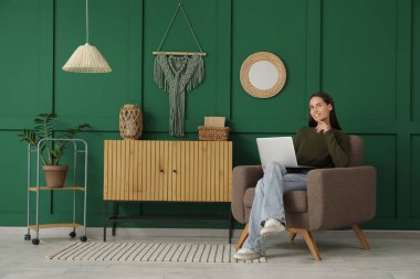 Evde koltukta otururken dizüstü bilgisayar kullanan genç kadın