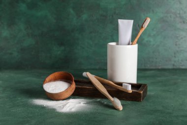 Bir kase diş pudrası, fırça, tutucu ve diş macunu yeşil grunge arka planda.