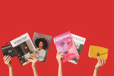 Farklı dergilere sahip kadın elleri ve kırmızı arka planda şık çantalar.