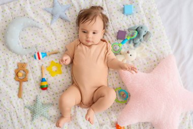 Battaniyenin üstünde oyuncakları olan şirin bir bebek.