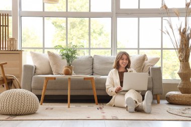 Oturma odasındaki kanepenin yanında dizüstü bilgisayarla sohbet eden genç bir kadın.