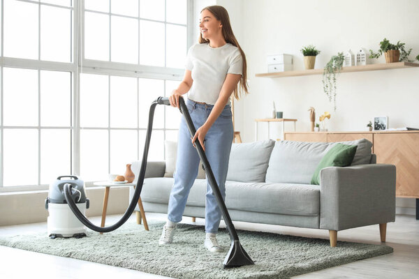 Young woman vacuuming carpet at home