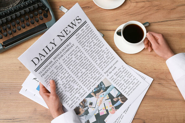 Руки женщины держат чашку кофе и газеты на деревянном фоне