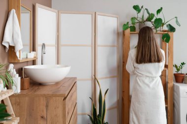 Banyoda bornozlu genç bir kadın.