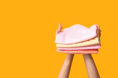 Sarı arka planda farklı giysi yığınları olan kadın elleri.