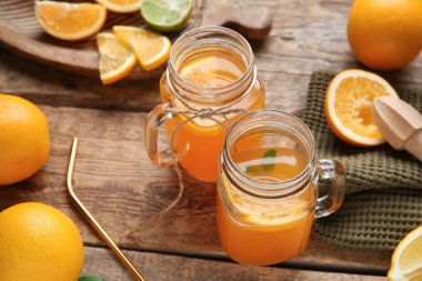 Mason kavanozları dolusu taze portakal suyu, farklı narenciye meyveleri ve tahta arka planda meyve sıkacağı.