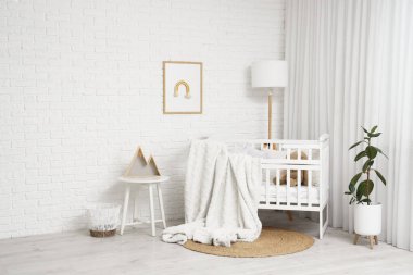 Çocuk odasının içindeki beyaz tuğla duvarın yanında ekose ve lambayla güzel bir beşik.