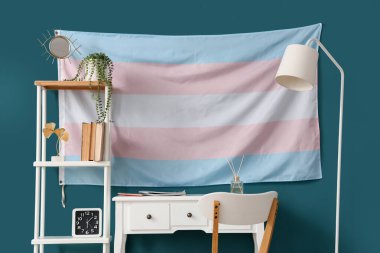 Masası, raf ünitesi ve transseksüel bayrağı olan odanın içi
