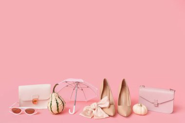 Şık çantaları, aksesuarları, şemsiyesi ve pembe arka planda balkabakları olan bej topuklu ayakkabılar.