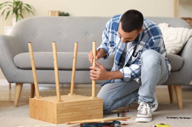 Genç adam evde ahşap masa kuruyor.
