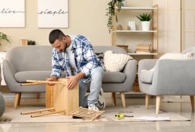 Genç adam evde ahşap masa kuruyor.